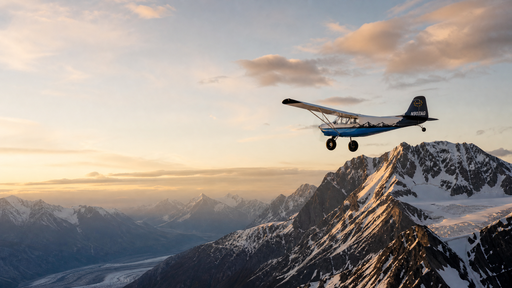 Super Pacer N907AG flying over rugged snow-capped Alaska mountains at golden hour
